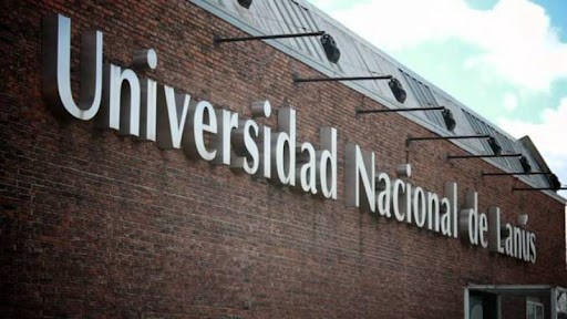La imagen muestra la pared frontal de uno de los edificios de la UNLa, observándose con letras mayúsculas y minúsculas el nombre de  la universidad: Universidad Nacional de Lanús